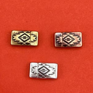 May include: Three rectangular metal clasps with a Southwestern design. One is gold-toned, one is copper-toned, and one is silver-toned. Each clasp features a geometric pattern in a contrasting color against a dark background.