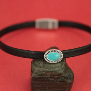 May include: A black leather choker necklace with a silver oval charm featuring a turquoise stone.
