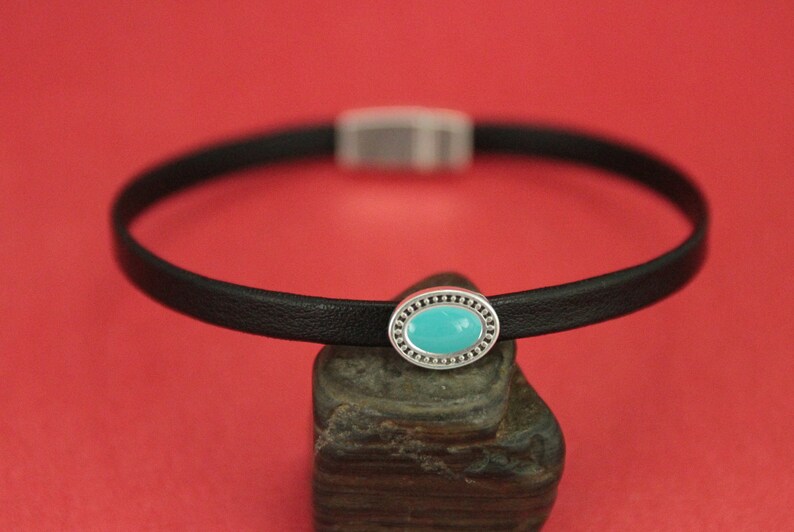 May include: A black leather choker necklace with a silver oval charm featuring a turquoise stone.