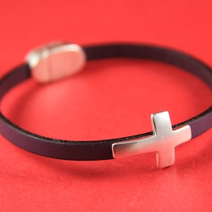 May include: A black leather bracelet with a silver cross charm and a silver magnetic clasp.