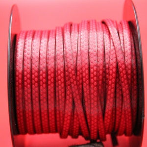 May include: A spool of red leather cord with a textured, dotted pattern. The cord is wound tightly around a black spool.