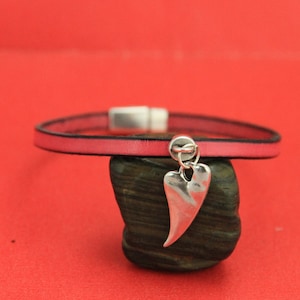May include: A pink leather bracelet with a silver heart charm. The bracelet has a magnetic clasp.
