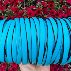 May include: A roll of turquoise blue leather cord with black edging. The cord is approximately 1/2 inch wide.