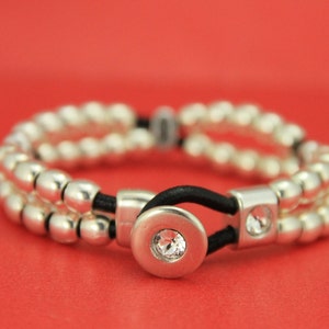 May include: A silver beaded bracelet with a black elastic band and a silver button closure with a clear crystal in the center.