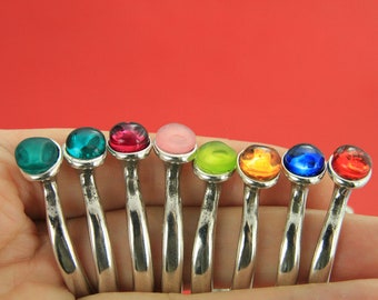Könnte beinhalten: Ein Satz von neun Silberringen mit bunten Glassteinen. Die Steine sind grün, rosa, rot, lindgrün, orange, blau und rot.