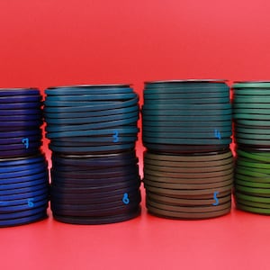 May include: Stacks of colorful leather strips in shades of blue, teal, green, and brown. Each roll is neatly coiled, showcasing the variety of colors available. The background is a solid red.