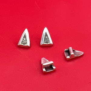 May include: Three silver triangle-shaped metal pieces with a decorative design. The pieces are on a red surface.