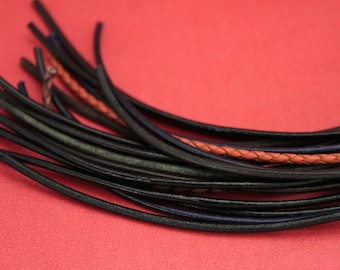 May include: A close-up of several black leather cords, some with blue or orange accents, against a red background. The cords are arranged in a curved, flowing pattern, suggesting a craft or jewelry-making theme.