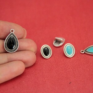 May include: Four silver-toned metal charms with black and turquoise enamel. Two charms are teardrop shaped and two are oval shaped.