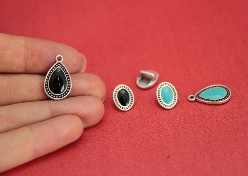 May include: Four silver-toned metal charms with black and turquoise enamel. Two charms are teardrop shaped and two are oval shaped.