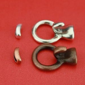 May include: Two silver and copper metal clasps with two matching half-circle pieces. The clasps have a ring and a hook-like shape.