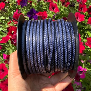May include: A spool of dark blue leather cord with a textured, dotted pattern. The cord is wound around a black plastic spool.