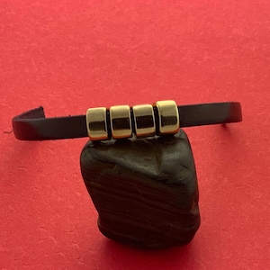 May include: A black leather bracelet with four gold-colored metal beads.
