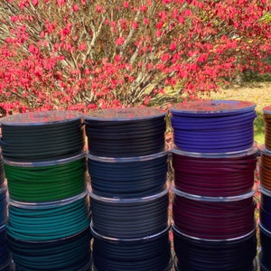 May include: A collection of spools of leather cord in various colours, including teal, green, navy, purple, burgundy, and orange. The spools are arranged in a row on a table.