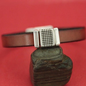 May include: A brown leather bracelet with a silver magnetic clasp. The clasp has a textured design.