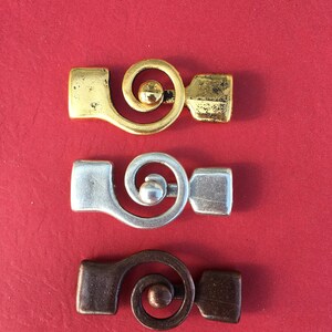 May include: Three metal clasps with a spiral design. The clasps are in gold, silver, and bronze.
