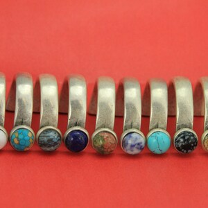 May include: A set of ten silver rings with different colored gemstones. The rings are all the same size and shape, and they are arranged in a row. The gemstones are red, white, blue, green, and brown.