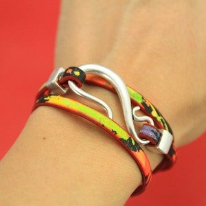 May include: A multi-layered bracelet with a silver hook clasp. The bracelet is made of black leather with colorful paint splatters in shades of orange, yellow, and green.