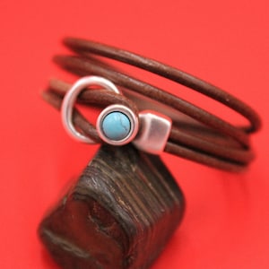 May include: A brown leather wrap bracelet with a silver clasp and a turquoise stone accent.