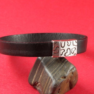 May include: A black leather bracelet with a silver heart-shaped clasp.