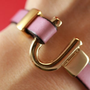 May include: A pink leather bracelet with a gold clasp and a large gold hook-shaped charm.