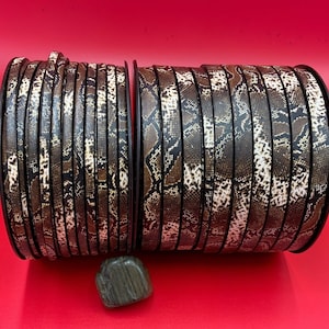 May include: Two spools of brown and beige faux snakeskin leather cord. The cord is wound tightly around each spool.