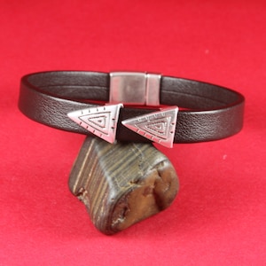 May include: A brown leather bracelet with two silver triangular charms. The charms have a geometric pattern.
