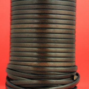 May include: A close-up of a roll of dark brown leather cord. The cord is tightly wound and has a smooth, polished finish.