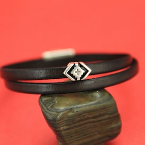 May include: A black leather wrap bracelet with a silver geometric charm. The bracelet is double-layered and has a simple design.