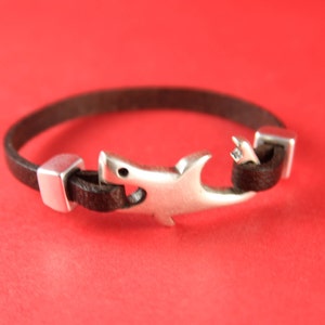 May include: A brown leather bracelet with a silver shark charm and silver metal clasps.