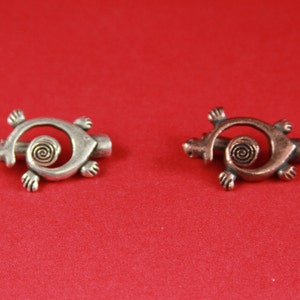 May include: Two turtle-shaped metal charms, one silver and one copper, with a spiral design on the shell.