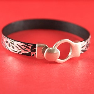 May include: A black leather bracelet with a silver clasp and a white floral design.