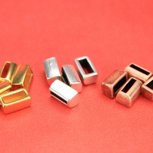 May include: A group of small metal clasps in gold, silver, and copper tones. The clasps are rectangular with a small opening in the center.