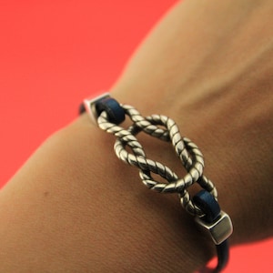May include: A silver knot bracelet with a blue leather band. The knot is a classic sailor's knot.
