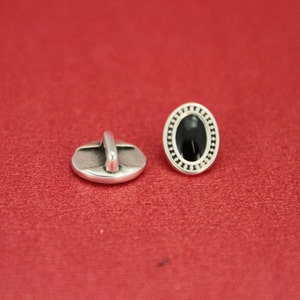 May include: Two silver oval buttons with a black center. One button has a decorative border and the other has a loop on the back.