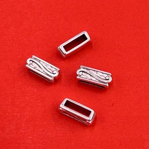 May include: Four silver-colored rectangular jewelry components with an open center and decorative wave design. The components are displayed on a red background.