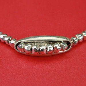 May include: A silver necklace with a unique, geometric design. The necklace features a series of small, silver beads that are connected by a thin, black cord. The beads are arranged in a pattern that resembles a row of teeth.