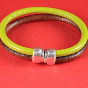 May include: A two-strand bracelet with a brown and lime green leather band. The bracelet is connected with a silver-colored magnetic clasp. The bracelet is shown on a red background.