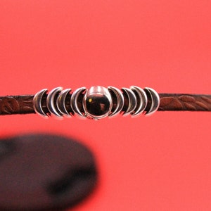 May include: A brown leather bracelet with a silver moon charm and a silver bead in the center.