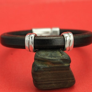 May include: A black leather bracelet with silver accents. The bracelet is made of a thick, durable leather and has a simple, elegant design.