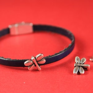 May include: A dark blue leather bracelet with a silver dragonfly charm and two silver clasp closures.