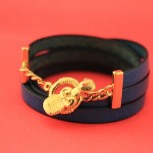 May include: A blue leather wrap bracelet with a gold-toned clasp featuring a decorative design.