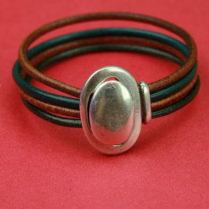 May include: A multi-layered bracelet with brown and green leather straps and a silver oval-shaped clasp.