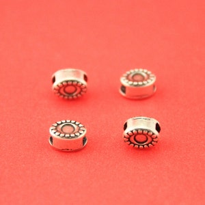 May include: Four silver-toned metal beads with a decorative design. Each bead has a circular center with a raised ring around it. The beads are arranged in a square pattern on a red background.