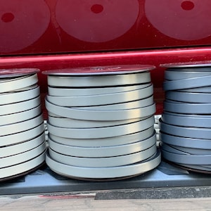 May include: Three spools of leather cord in different shades of gray. The spools are stacked on top of each other and are in focus. The background is blurred and out of focus.