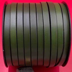 May include: A roll of dark green leather cord, wound around a black spool. The cord is approximately 1/4 inch wide.