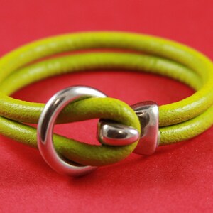 K&ouml;nnte beinhalten: Ein limegr&uuml;nes Lederarmband mit einem silbernen Metallverschluss. Der Verschluss ist ein einfacher Schlaufe.