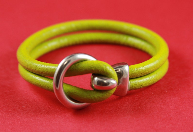 K&ouml;nnte beinhalten: Ein limegr&uuml;nes Lederarmband mit einem silbernen Metallverschluss. Der Verschluss ist ein einfacher Schlaufe.