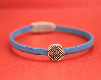 May include: A blue leather bracelet with a silver, patterned, round charm.
