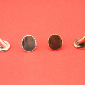 May include: Four metal eyelets in different finishes: silver, nickel, copper, and brass. The eyelets are on a red background.